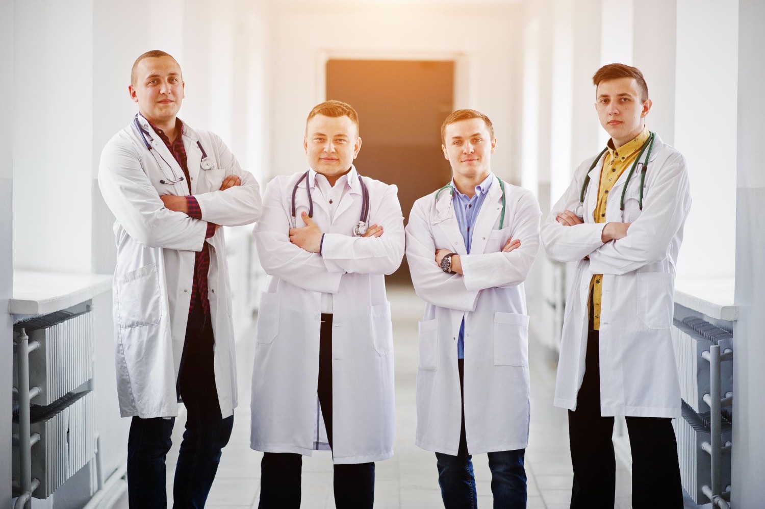 four-confident-male-doctors-white-coats-with-stethoscopes-standing-hallway-hospital