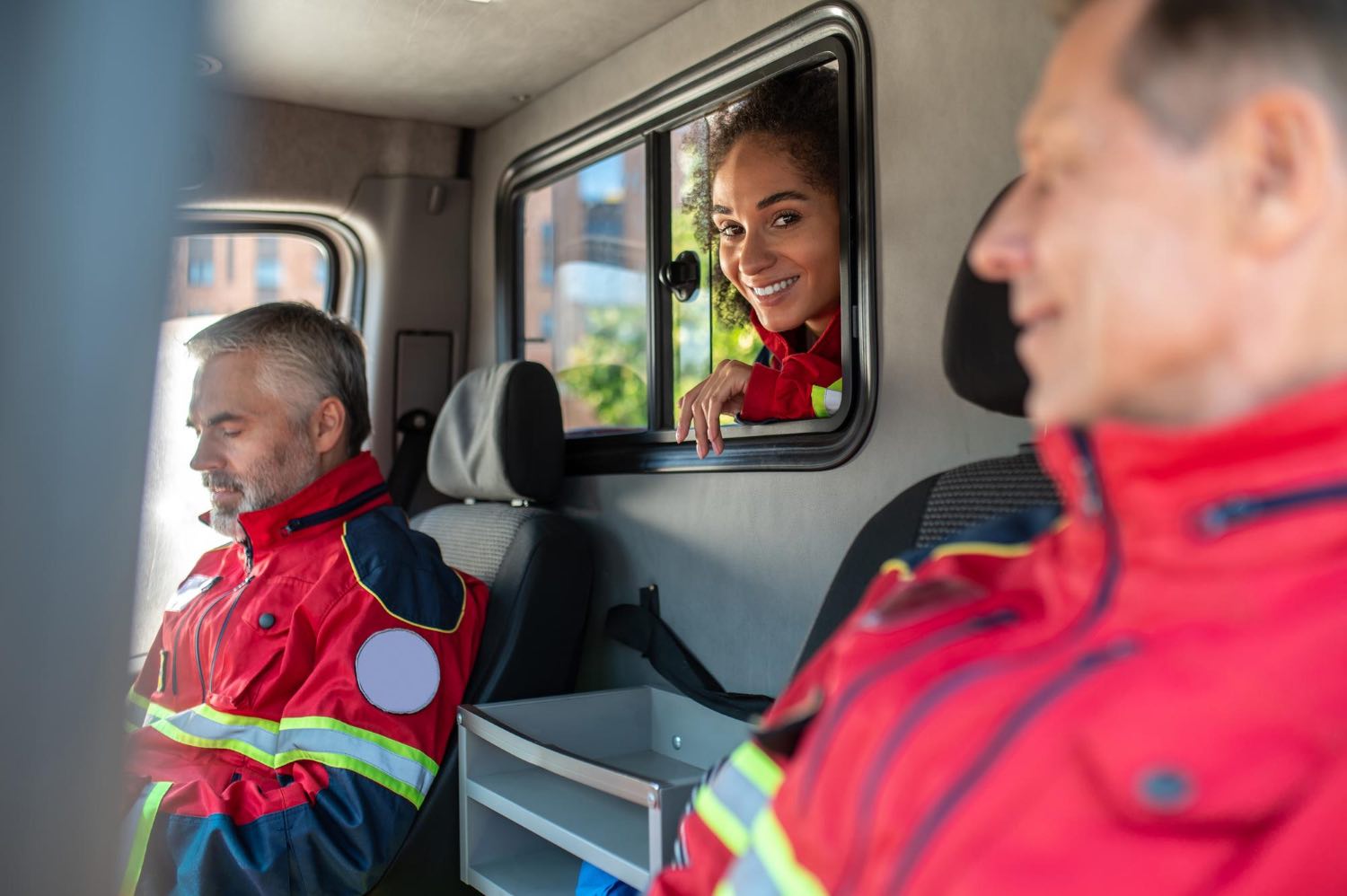 team-smiling-pleased-paramedics-red-uniforms-sitting-together-medical-emergency-vehicle